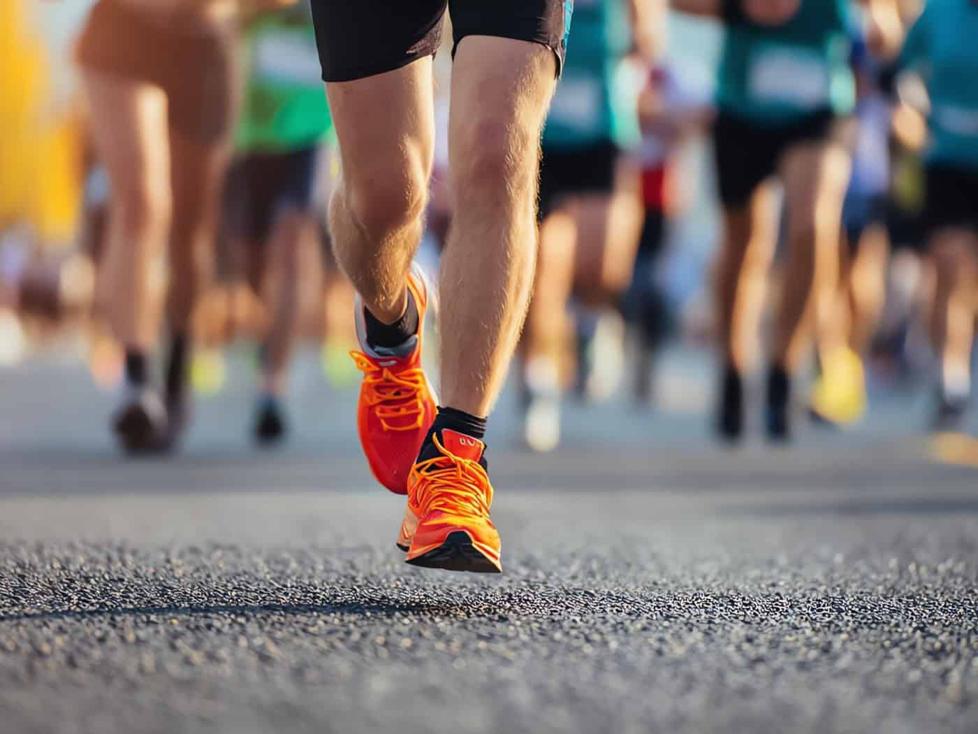 Läuferbeine mit orangefarbenen Laufschuhen im Marathon – Symbol für Ausdauer und Bewegung.