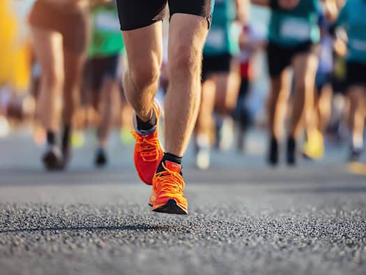Läuferbeine mit orangefarbenen Laufschuhen im Marathon – Symbol für Ausdauer und Bewegung.
