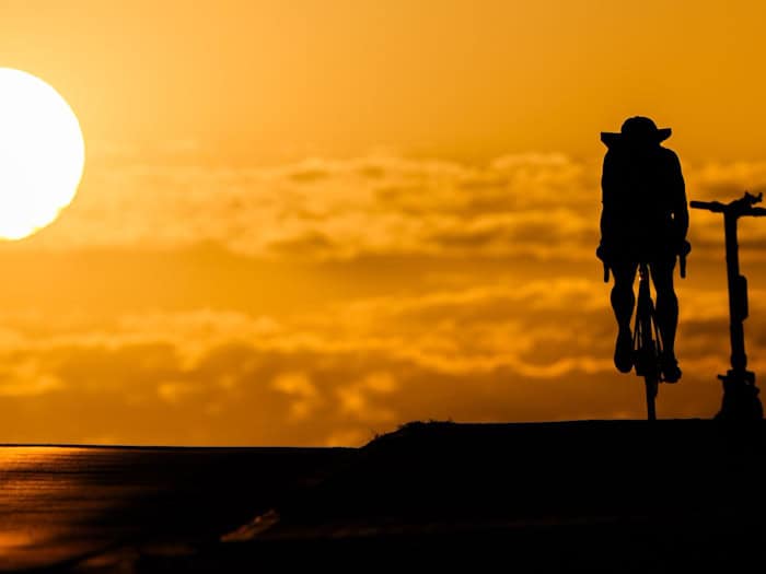 Ein Fahrradfahrer fährt bei Sonnenaufgang über eine Brücke in der Region Hannover. Hitze ist besonders am Nachmittag gefährlich. (Symbolbild) / Foto: Julian Stratenschulte/dpa