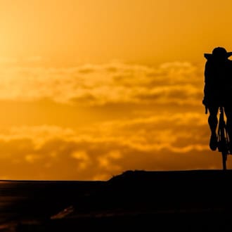 Ein Fahrradfahrer fährt bei Sonnenaufgang über eine Brücke in der Region Hannover. Hitze ist besonders am Nachmittag gefährlich. (Symbolbild) / Foto: Julian Stratenschulte/dpa