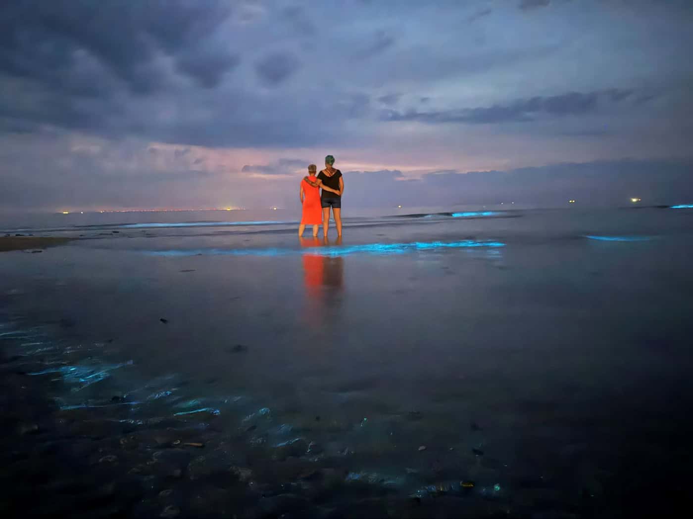 Im flachen Wasser beobachten zwei Frauen Meeresleuchten am Nordstrand von Norderney.  / Foto: Volker Bartels/dpa
