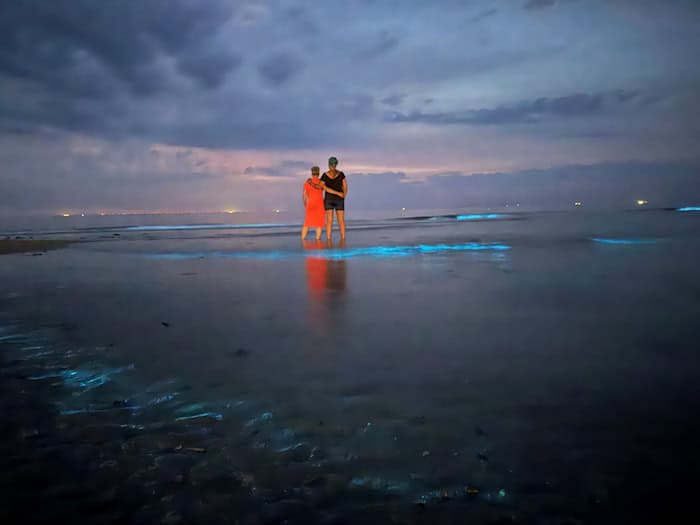 Im flachen Wasser beobachten zwei Frauen Meeresleuchten am Nordstrand von Norderney.  / Foto: Volker Bartels/dpa