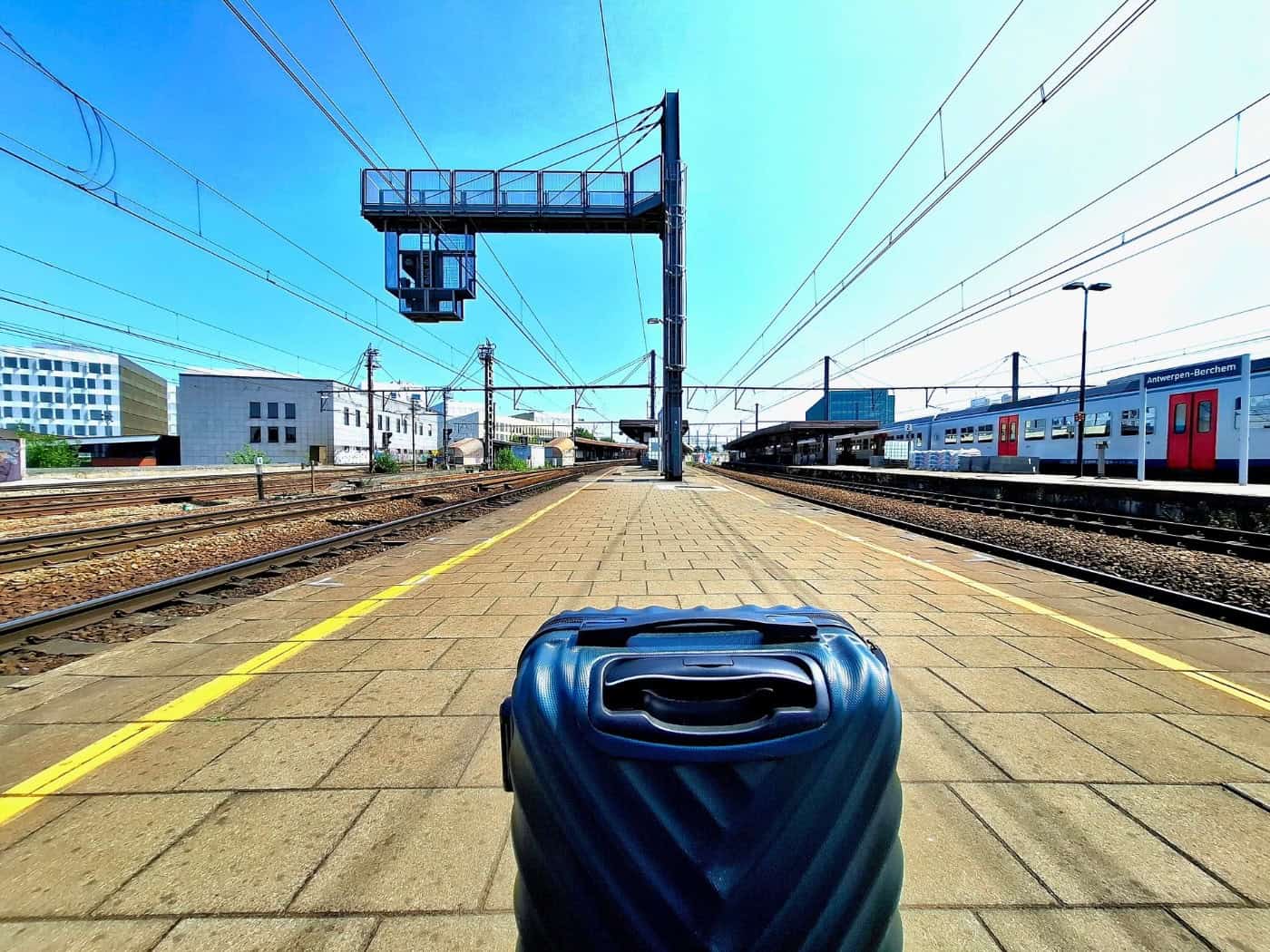 Blauer Koffer auf einem Bahnsteig mit Zug im Hintergrund und klarem Himmel