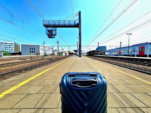 Blauer Koffer auf einem Bahnsteig mit Zug im Hintergrund und klarem Himmel