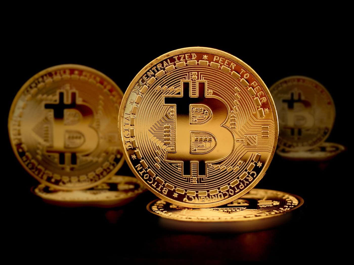 Goldfarbene Bitcoin-Münzen mit dem typischen "B"-Symbol, gestapelt auf einem glänzenden Untergrund mit dramatischer Beleuchtung.