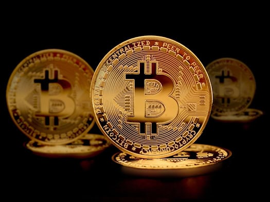 Goldfarbene Bitcoin-Münzen mit dem typischen "B"-Symbol, gestapelt auf einem glänzenden Untergrund mit dramatischer Beleuchtung.