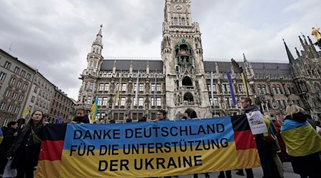 Teilnehmer einer Kundgebung anlässlich des zweiten Jahrestags des russischen Angriffskriegs auf die Ukraine stehen mit einem Banner «Danke Deutschland für die Unterstützung der Ukraine» auf dem Marienplatz. / Foto: Uwe Lein/dpa