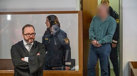 Der Angeklagte (r) wird in den Gerichtssaal geführt. Der Rechtsanwalt des Angeklagten, Maximilian Siller (l), steht an seinem Platz. / Foto: Daniel Vogl/dpa