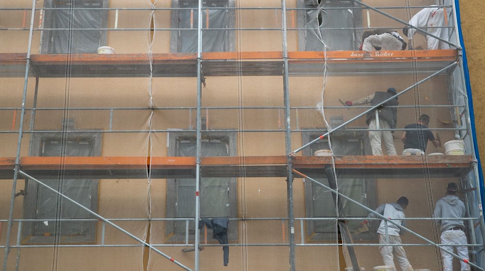 Arbeiter auf einem Baugerüst verrichten Arbeiten an der Fassade eines Hauses. / Foto: Daniel Karmann/dpa