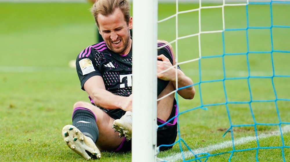 Harry Kane von München sitzt mit schmerzverzerrtem Gesicht auf dem Rasen. Er will gegen Dortmund spielen. / Foto: Uwe Anspach/dpa