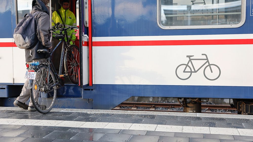 Ein Mann muss sein Fahrrad in den Zug heben. / Foto: Daniel Löb/dpa