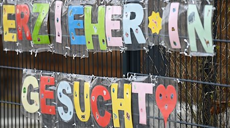 Mit bunten Buchstaben sind die Worte „Erzieher*in gesucht“ geformt, die an einem Zaun einer Kindertagesstätte befestigt sind. / Foto: Arne Dedert/dpa