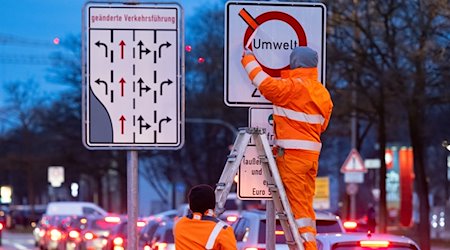 Arbeiter entfernen einen roten Klebestreifen von einem Schild. / Foto: Sven Hoppe/dpa