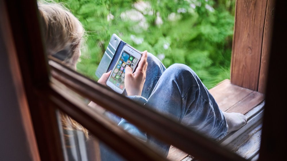 Ein Junge sitzt am Fenster und schaut auf sein Handy. / Foto: Annette Riedl/dpa/Symbolbild