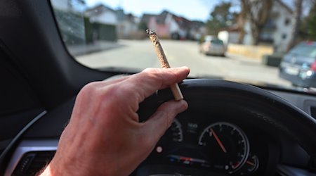 Ein Mann sitzt mit einem Joint zwischen den Fingern am Steuer eines Autos. / Foto: Karl-Josef Hildenbrand/dpa