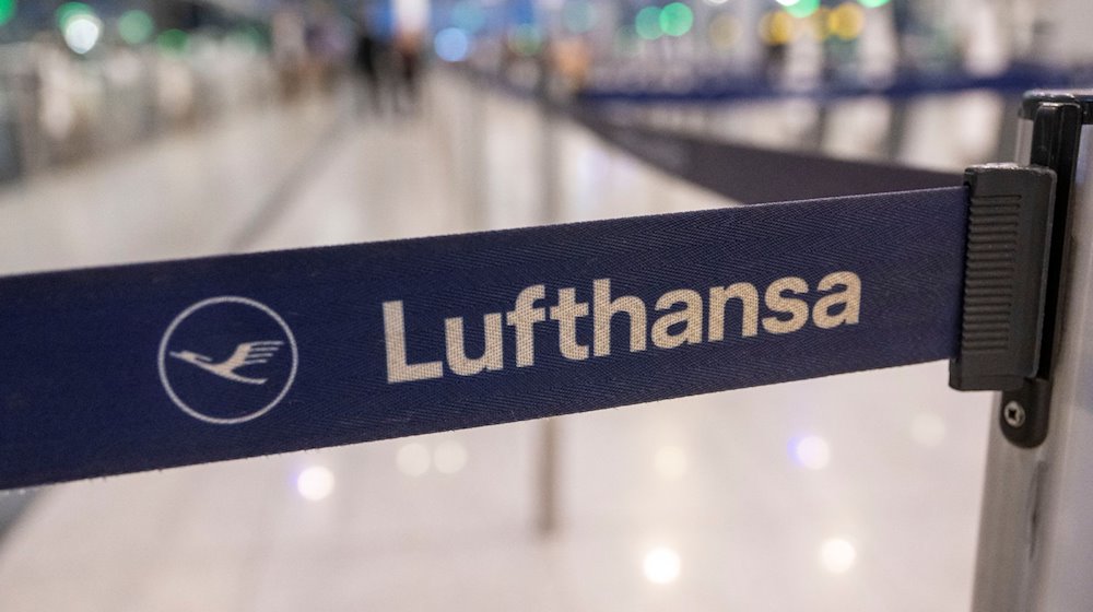 Das Logo der Lufthansa ist auf einem Absperrband am Check-In am Flughafen zu sehen. / Foto: Peter Kneffel/dpa