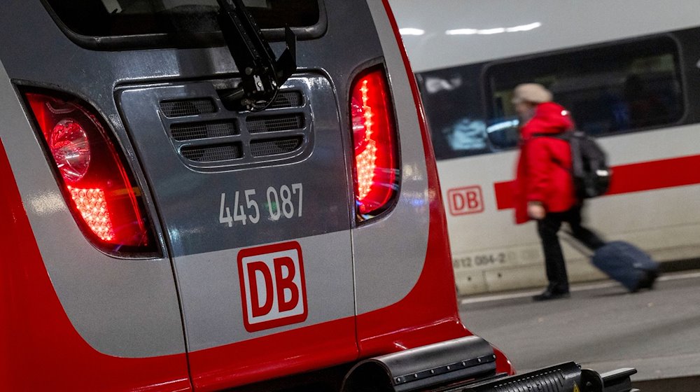 Eine Regionalbahn und ein ICE der Deutschen Bahn stehen nebeneinander im Hauptbahnhof, während eine Frau mit einem Koffer vorbeiläuft. / Foto: Peter Kneffel/dpa