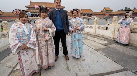 Markus Söder besucht die historische verbotene Stadt in der chinesischen Hauptstadt und steht neben Frauen in traditionellen Kostümen. / Foto: Peter Kneffel/dpa
