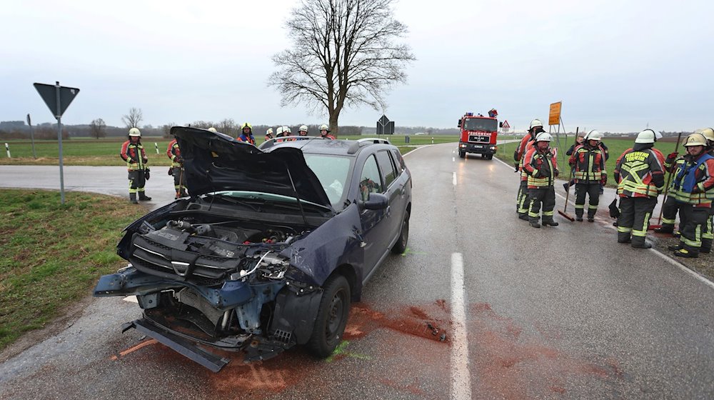 Einsatzkräfte der Feuerwehr stehen neben einem beschädigten Auto an der Unfallstelle. / Foto: Karl-Josef Hildenbrand/dpa