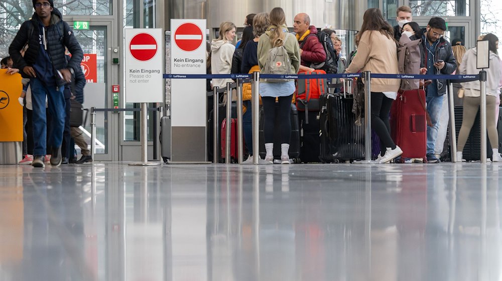 Passagiere stehen in der Abflughalle in Schlangen am Check-in an. / Foto: Peter Kneffel/dpa
