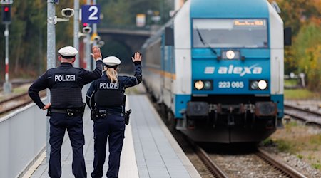 Bundespolizisten weisen per Handzeichen den Lokführer eines Zuges aus Prag in Richtung München darauf hin, dass sie zusteigen werden. / Foto: Daniel Karmann/dpa/Archivbild