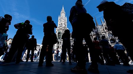 Touristen und Einheimische verfolgen das Glockenspiel auf dem Marienplatz in München. / Foto: Sven Hoppe/dpa