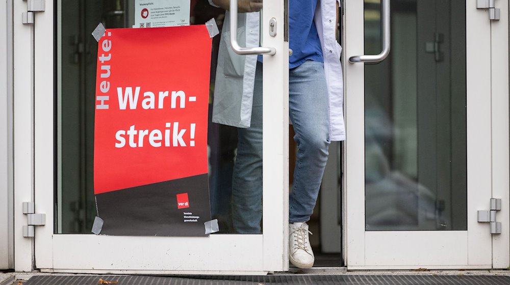 Ein Plakat mit der Aufschrift «Heute Warnstreik» hängt am Eingang eines Gebäudes. / Foto: Marijan Murat/dpa