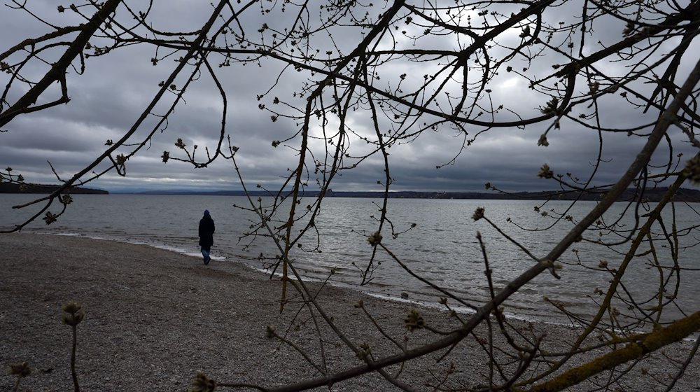 Ein Ausflügler läuft am Ufer des wolkenverhangenen Ammersees. / Foto: Karl-Josef Hildenbrand/dpa