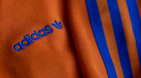 Das Logo des Sportartikelherstellers adidas in blau auf einer orangen Jacke. / Foto: Daniel Karmann/dpa