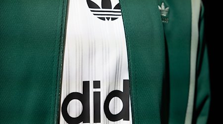 Das Logo und der Schriftzug von Adidas ist auf einem ausgestellten Kleidungsstück zu sehen. / Foto: Daniel Karmann/dpa/Symbolbild