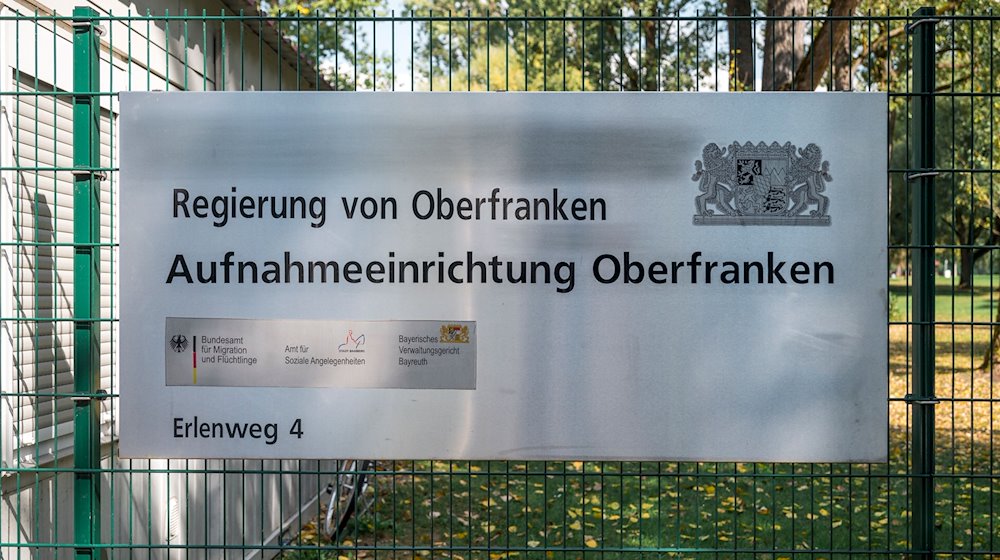 Ein Hinweisschild der Aufnahmeeinrichtung Oberfranken hängt am Zaun der Flüchtlingsunterkunft. / Foto: Daniel Vogl/dpa