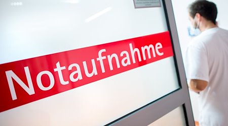 Ein Krankenpfleger steht in einem Krankenhaus neben einer Glastür mit der Aufschrift «Notaufnahme». / Foto: Hauke-Christian Dittrich/dpa