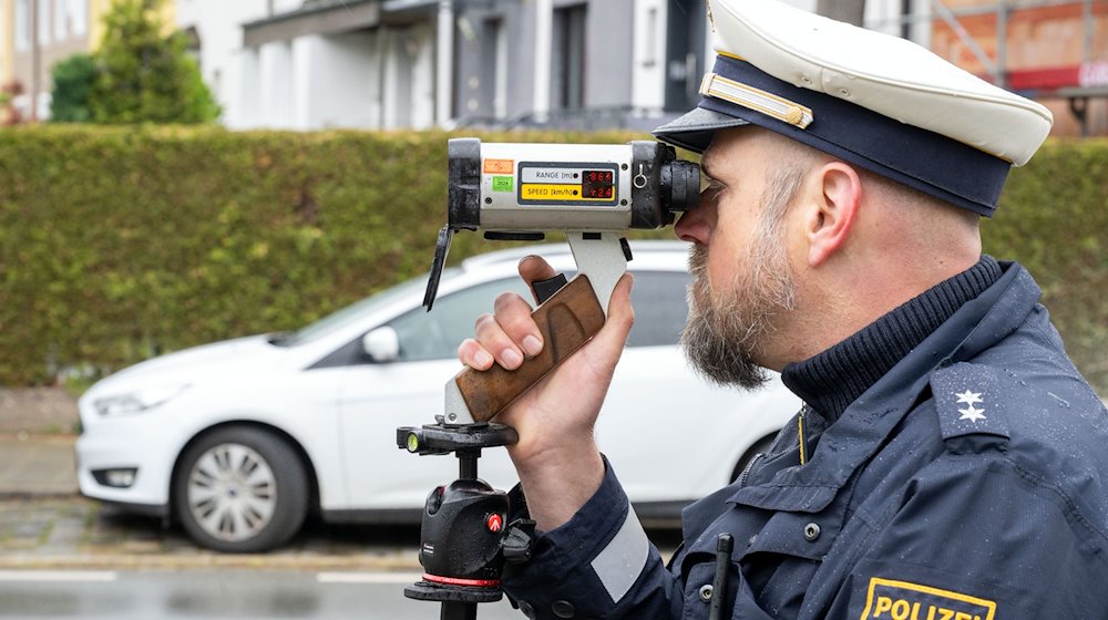 Ein Polizeibeamter schaut durch ein Messgerät zur Geschwindigkeitskontrolle. / Foto: Pia Bayer/dpa