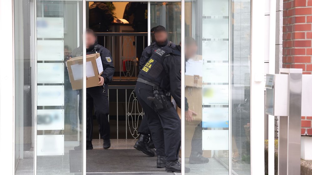 Polizeibeamte tragen in Kartons sichergestelltes Material aus einem Gebäude. / Foto: Gianni Gattus/dpa