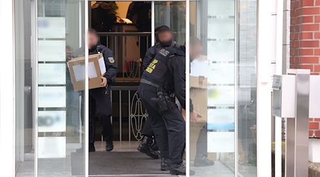 Polizeibeamte tragen in Kartons sichergestelltes Material aus einem Gebäude. / Foto: Gianni Gattus/dpa