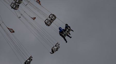 Besucher sitzen vor starkt bewölktem Himmel in einem Fahrgeschäft des Stuttgarter Frühlingsfestes. / Foto: Marijan Murat/dpa