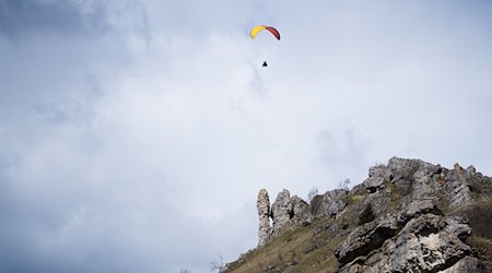 Ein Paraglider fliegt bei teilweise blauem Himmel an einem Berg vorbei. / Foto: Nicolas Armer/dpa