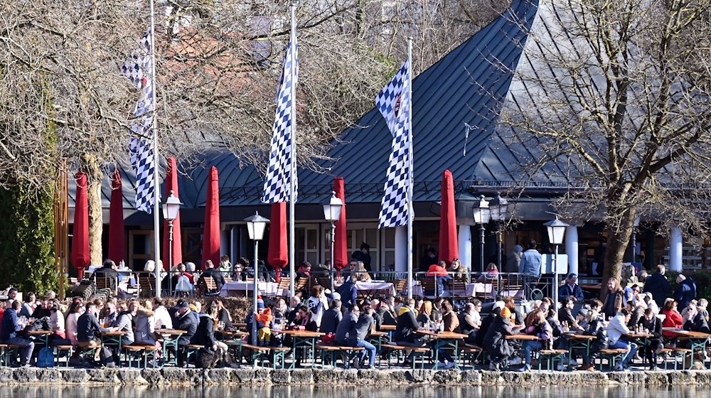 Zahlreiche Menschen sitzen in einem Biergarten im Englischen Garten am Kleinhesseloher See und genießen die Sonne. / Foto: Katrin Requadt/dpa/Archivbild