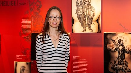 Die Museumsleiterin und Kuratorin Christine Demele steht vor einer Ausstellungstafel mit Fotografien von Tätowierungen, die nach Kunstwerken von Albrecht Dürer entstanden sind. / Foto: Oliver Frank/Albrecht-Dürer-Haus/dpa