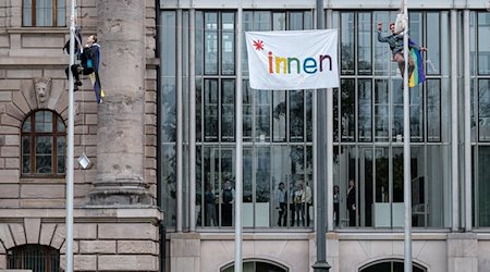 Zwei Menschen haben einen Fahnenmast vor der Bayerischen Staatskanzlei in München erklommen, um gegen das bayerische Genderverbot zu demonstrieren. / Foto: Thomas Vonier/SZ/dpa