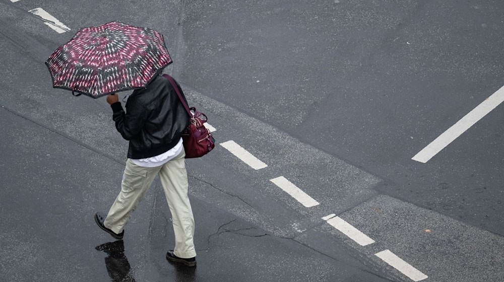 Mit einem Schirm schützt sich eine Passantin vor dem strömenden Regen. / Foto: Boris Roessler/dpa/Symbolbild