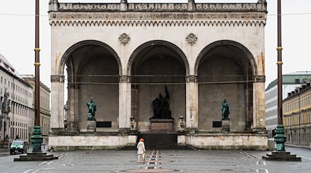 Eine Frau geht über den menschenleeren Odeonsplatz an der Feldherrnhalle vorüber. Am Donnerstag soll dort das Projekt «Die Rückkehr der Namen» seinen Abschluss finden. / Foto: Matthias Balk/dpa/Archivbild