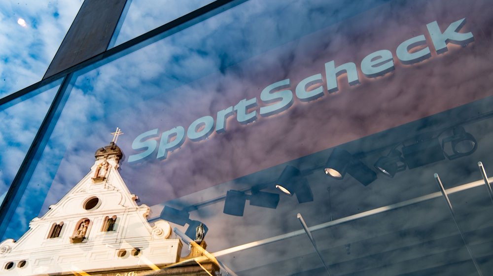 In der Fassade einer SportScheck-Filiale in der Münchener Fußgängerzone spiegelt sich ein Haus. / Foto: Lino Mirgeler/dpa
