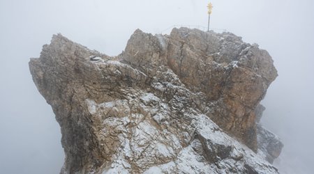 Nebelwolken umhüllen bei Schneetreiben auf der Zugspitze (2962 Meter) die verschneite Aussichtsplattform mit dem Gipfelkreuz. / Foto: Peter Kneffel/dpa/Archivbild