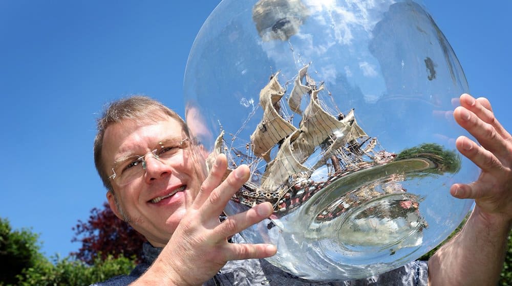 Matthias Schultz hält ein von ihm gebautes 40 Zentimeter hohes und 38 Zentimeter langes Buddelschiff welches in einem 50 Liter fassenden Gärballon hängt. / Foto: Karl-Josef Hildenbrand/dpa