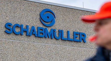 Schwabmüller ist an einem Firmengebäude hinter einem streikenden Mitarbeiter angebracht. / Foto: Armin Weigel/dpa/Archivbild