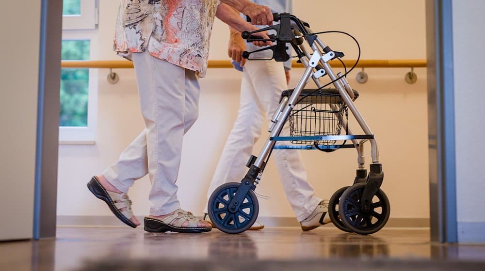 Eine Pflegekraft geht in einem Pflegeheim mit einer älteren Dame über einen Korridor. / Foto: Christoph Schmidt/dpa