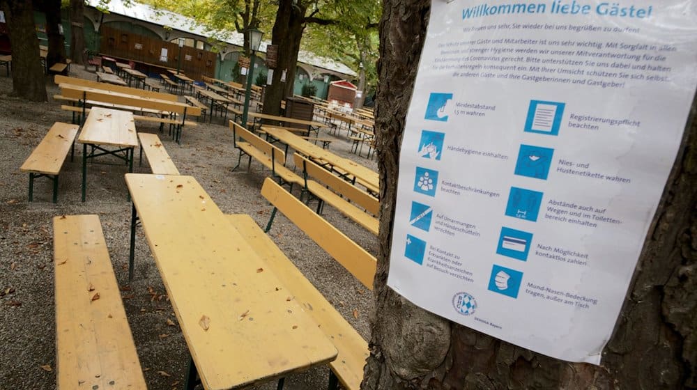 Ein Hinweisschild mit Corona-Restriktionen im Oktober 2020 am Baum eines leeren Biergartens. / Foto: Peter Kneffel/dpa