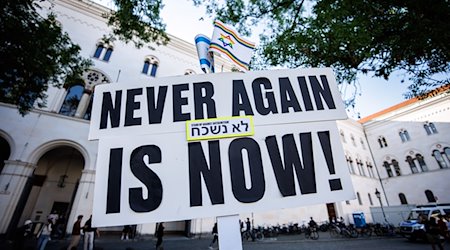 Ein Schild mit der Aufschrift „Never again is now!“ ist bei Teilnehmern einer Mahnwache gegen ein geplantes Pro-Palästina-Protestcamp vor der Ludwig-Maximilians-Universität (LMU) zu sehen. / Foto: Matthias Balk/dpa
