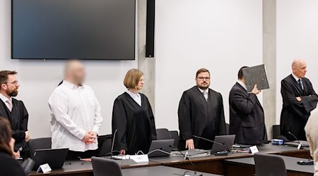 Zwei wegen Mordes angeklagte Männer (2.v.l.) und (2.v.r.) stehen zu Prozessbeginn im Sitzungssaal im Landgericht Nürnberg-Fürth zwischen ihren Anwälten. / Foto: Daniel Karmann/dpa
